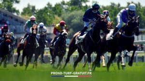 Horse race scene with several jockeys in colorful silks riding fast horses on a track; foreground shows green grass and a banner text 'PRONO-TURF-GRATUIT.FR' at the bottom.